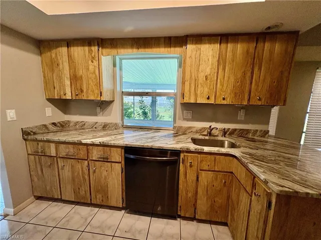Kitchen featuring light stone countertops, sink, light tile patterned floors, and dishwasher