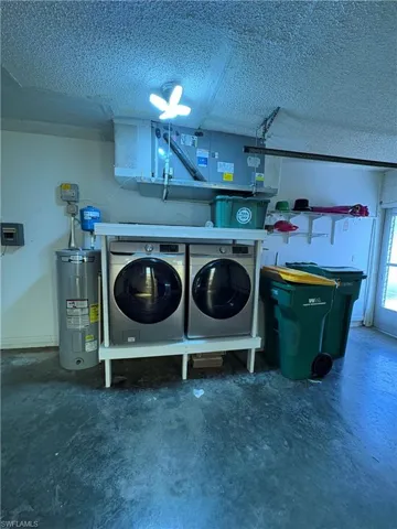 Clothes washing area featuring water heater, independent washer and dryer, and a textured ceiling