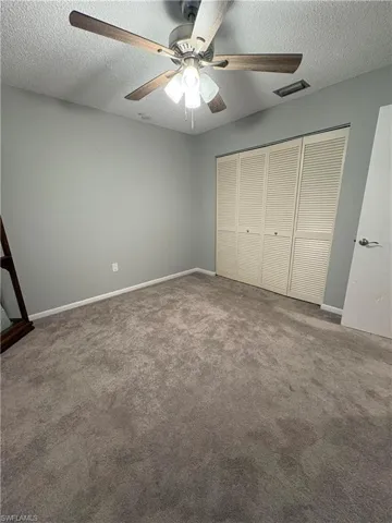 Unfurnished bedroom featuring ceiling fan, a textured ceiling, carpet floors, and a closet
