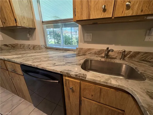 Kitchen featuring dishwasher, light stone countertops, sink, and light tile patterned flooring