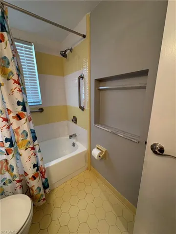 Bathroom featuring tile patterned flooring, toilet, and shower / bathtub combination with curtain