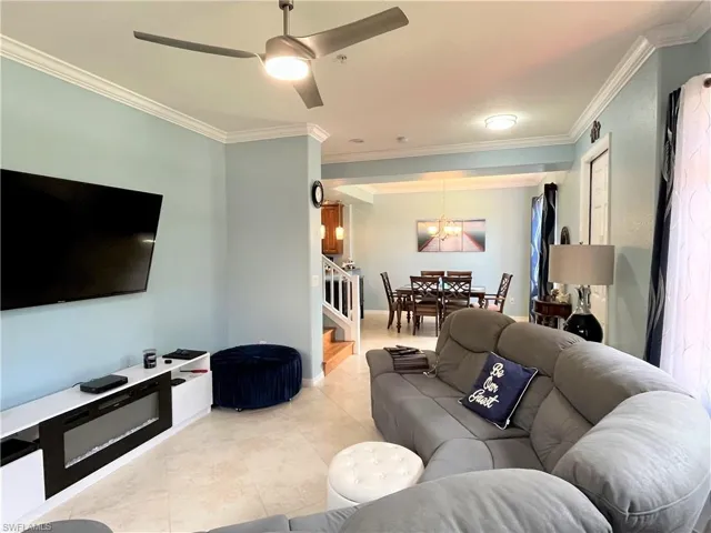 Living area with ceiling fan with notable chandelier, light tile patterned floors, ornamental molding, and stairs