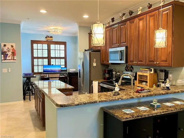 Kitchen featuring stone countertops, a peninsula, crown molding, brown cabinets, and appliances with stainless steel finishes