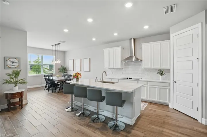 Kitchen with wall chimney exhaust hood, a sink, backsplash, black electric cooktop, and white cabinetry