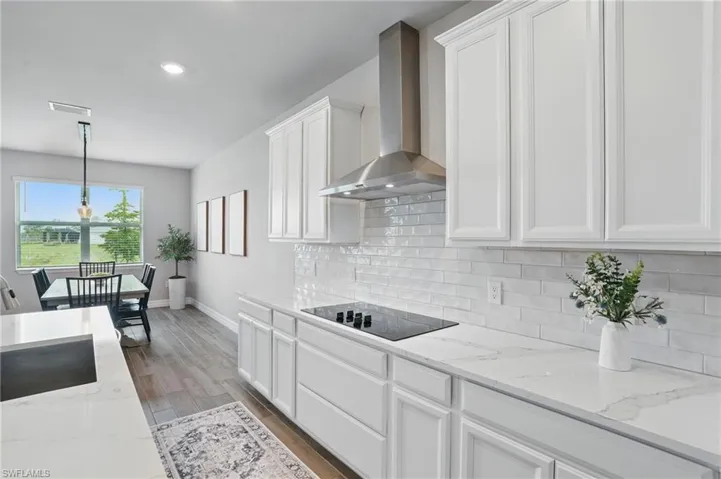 Kitchen with wall chimney exhaust hood, black electric cooktop, white cabinets, decorative backsplash, and recessed lighting