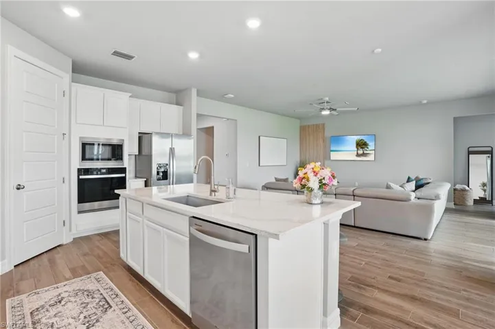 Kitchen featuring appliances with stainless steel finishes, a sink, open floor plan, a kitchen island with sink, and light wood-style floors