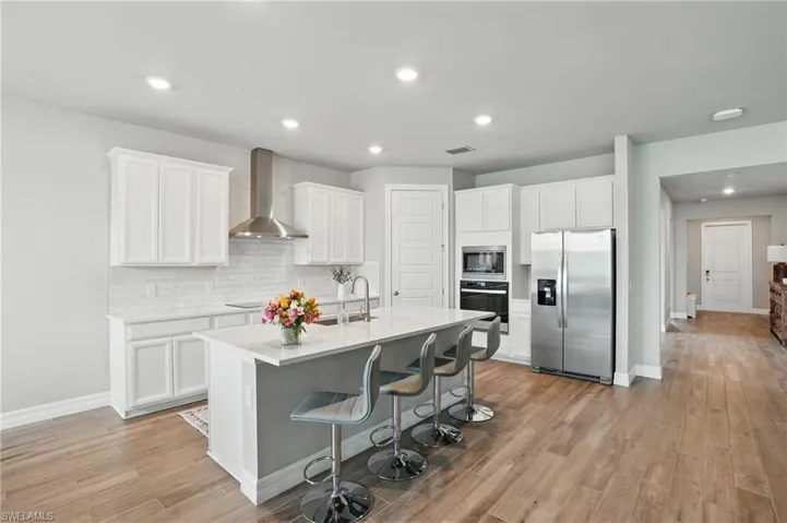 Kitchen with black appliances, wall chimney exhaust hood, a sink, light wood-type flooring, and recessed lighting