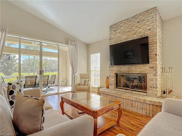 Living room featuring laminate floors, lofted ceiling, and a brick fireplace