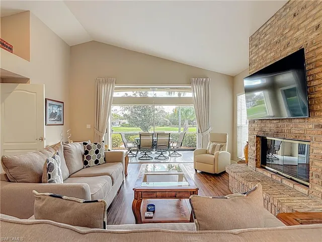 Living area with pocket sliders opening up to the screened lanai with a fireplace, laminate floors, and lofted ceiling
