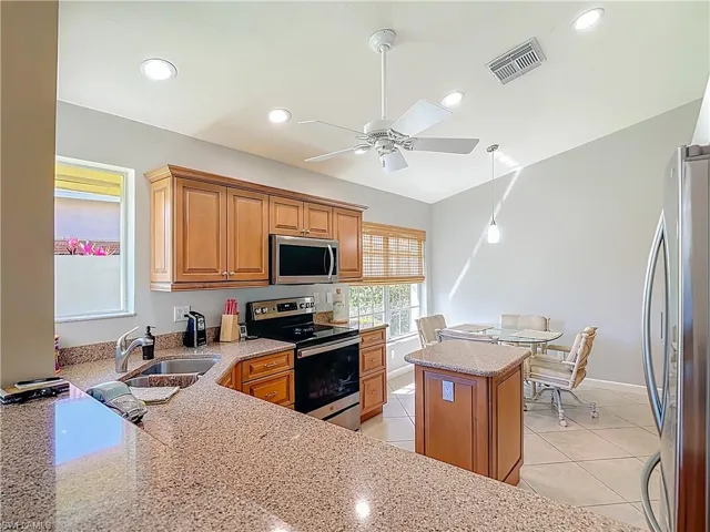 Kitchen featuring stainless steel appliances, light stone counters, a kitchen island, ceiling fan, and light tile patterned floors