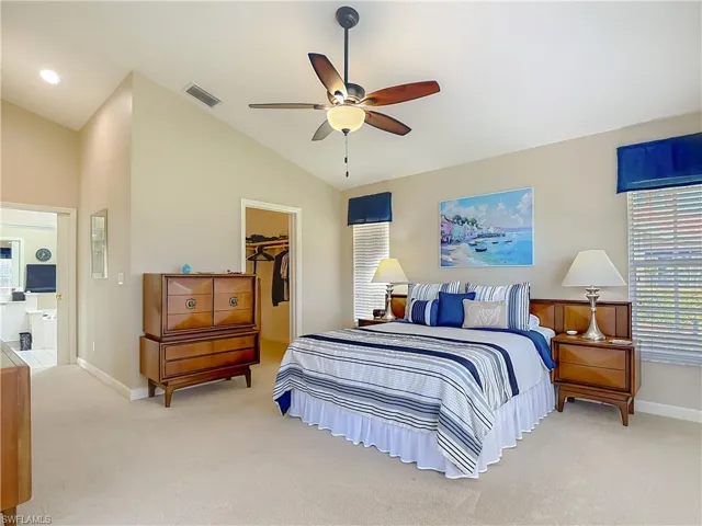 Primary Bedroom featuring a spacious closet, light colored carpet, ceiling fan, and vaulted ceiling