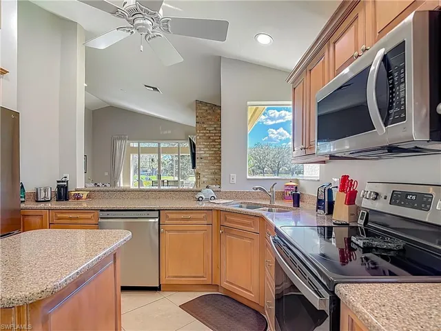 Kitchen with stainless steel appliances, light stone counters, vaulted ceiling, light tile patterned floors, and a ceiling fan