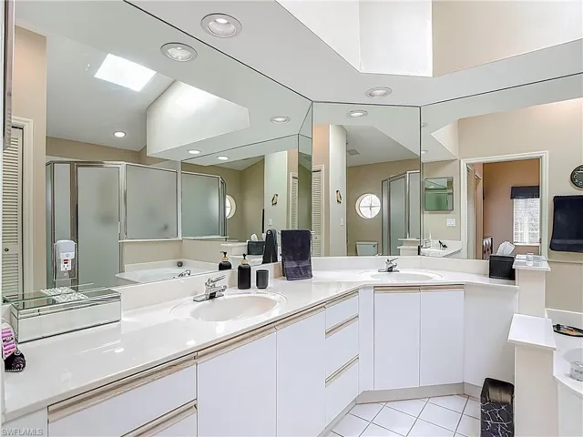 Full bath featuring a closet, double vanity, light tile patterned floors, a stall shower, and a skylight