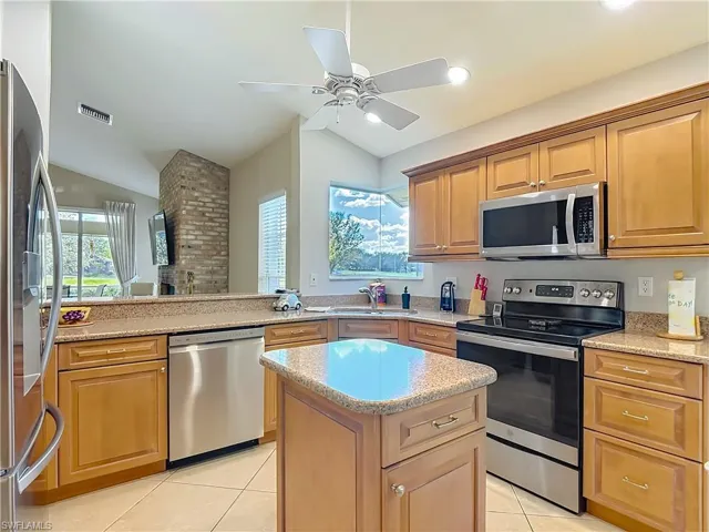 Kitchen with stainless steel appliances, light stone counters, a peninsula, vaulted ceiling, and light tile patterned floors