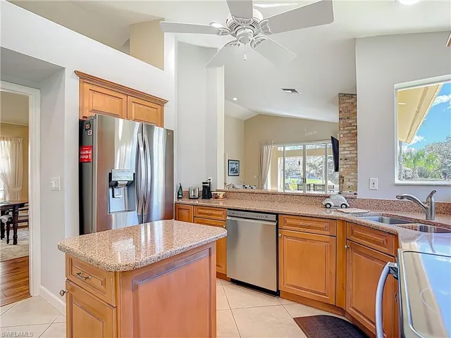 Kitchen featuring stainless steel appliances, light stone countertops, a ceiling fan, a kitchen island, and light tile patterned flooring