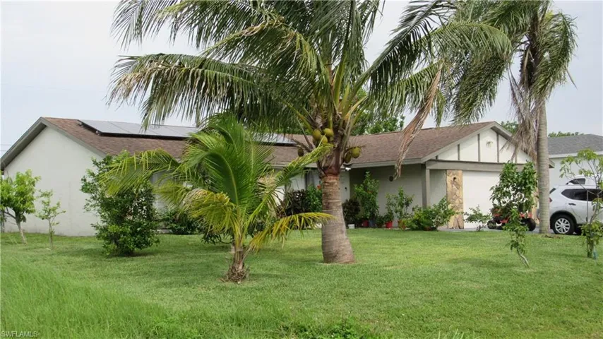 View of front of house with solar panels, stucco siding, a front yard, and a shingled roof