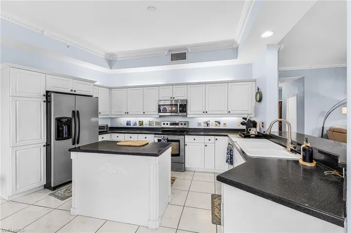 Kitchen featuring appliances with stainless steel finishes, white cabinetry, ornamental molding, dark countertops, and a center island