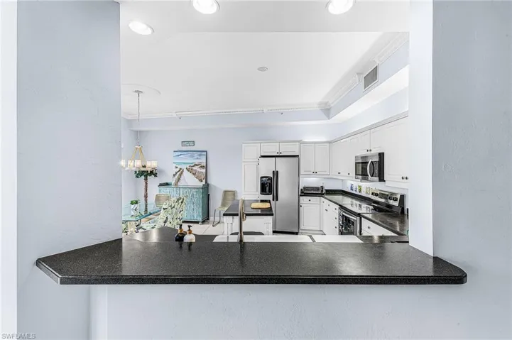Kitchen with dark countertops, a textured wall, appliances with stainless steel finishes, white cabinets, and a chandelier