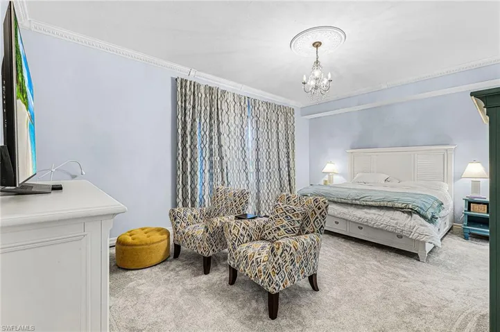Bedroom with light colored carpet, ornamental molding, and a chandelier