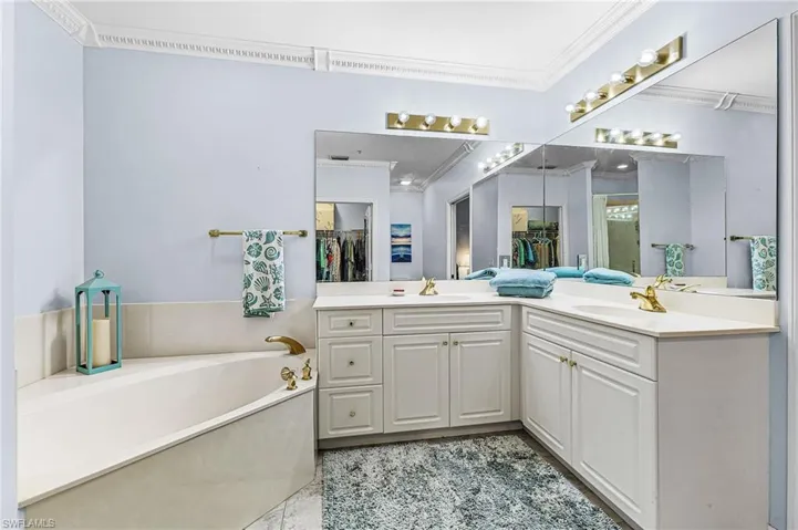 Full bath featuring double vanity, a garden tub, ornamental molding, and a walk in closet