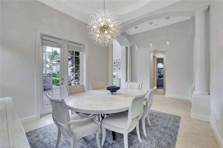 Dining space featuring french doors, ornate columns, arched walkways, a chandelier, and light tile patterned floors