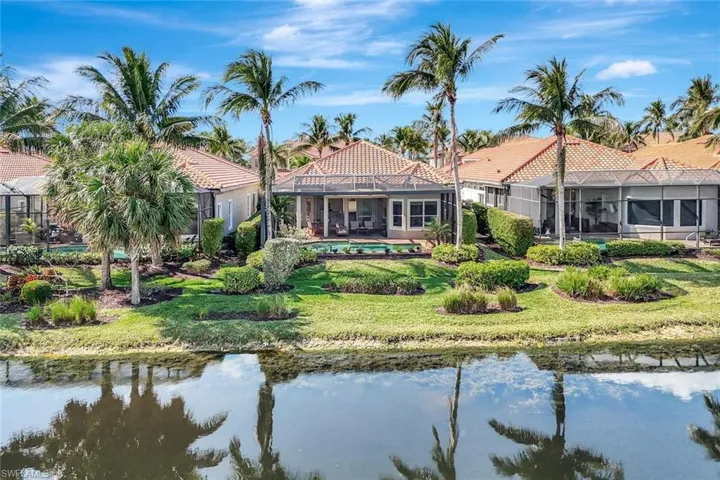 Rear view of property featuring a water view, a sunroom, glass enclosure, a patio area, and a lawn