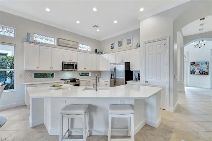 Kitchen with backsplash, light tile patterned floors, white cabinets, arched walkways, and ornamental molding