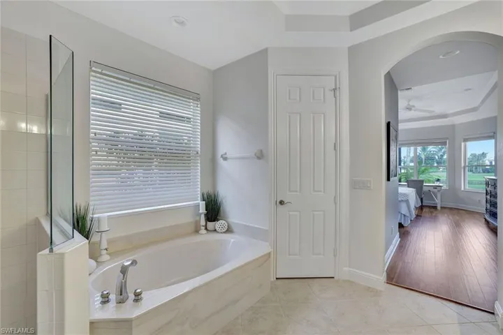 Ensuite bathroom featuring a raised ceiling, a garden tub, a shower stall, light tile patterned floors, and recessed lighting