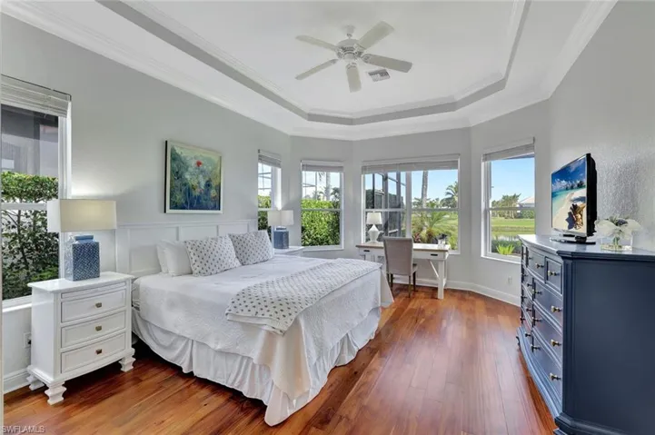 Bedroom with wood finished floors, a desk, crown molding, a tray ceiling, and ceiling fan