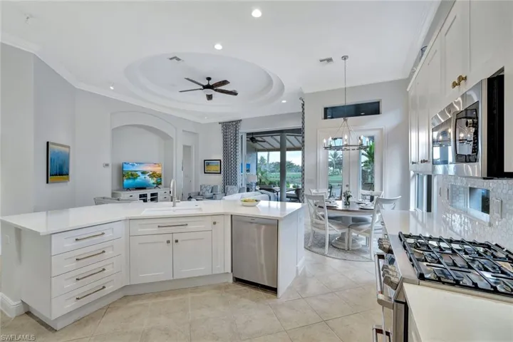 Kitchen featuring white cabinets, stainless steel appliances, pendant lighting, open floor plan, and light stone counters