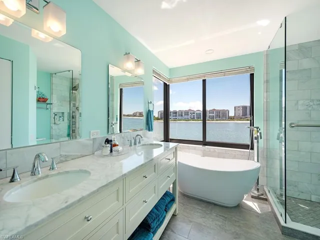 Bathroom with a stall shower, a freestanding bath, double vanity, a water view