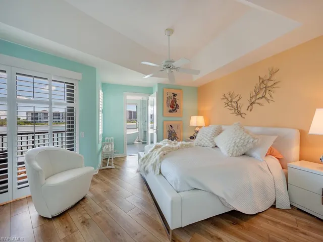 Bedroom featuring a raised ceiling, multiple windows, light wood-style flooring, and a ceiling fan