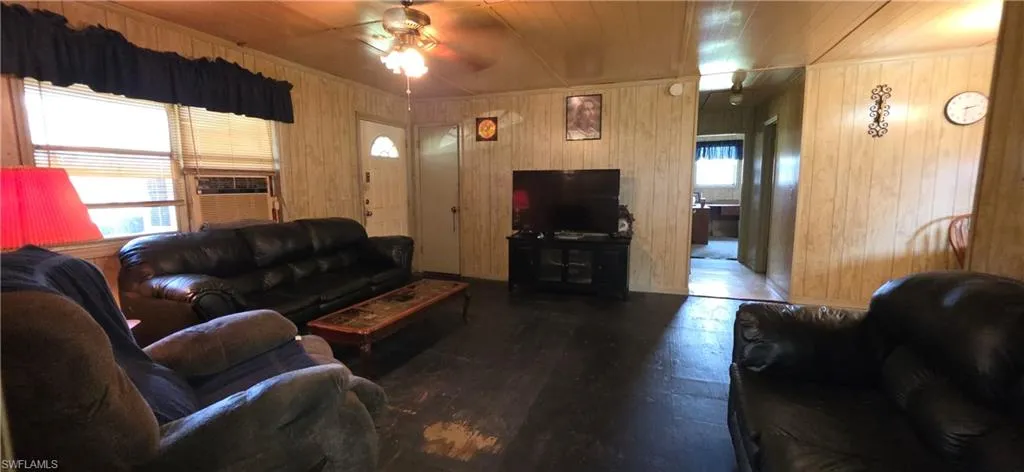 Living area featuring wood paneling, dark flooring, and a ceiling fan with integrated lighting