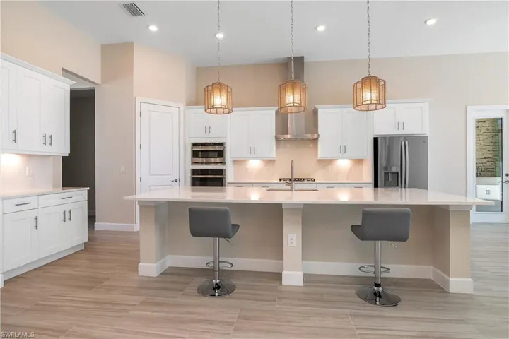 Kitchen with stainless steel appliances, a large island with sink, backsplash, hanging light fixtures, and white cabinets