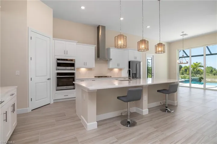 Kitchen featuring appliances with stainless steel finishes, white cabinets, a kitchen island with sink, wall chimney exhaust hood, and backsplash