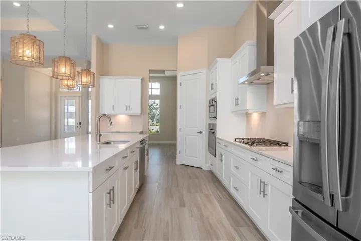 Kitchen with wall chimney range hood, white cabinetry, stainless steel appliances, sink, and tasteful backsplash