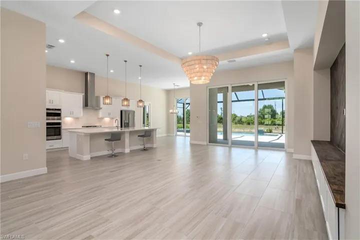 Unfurnished living room with an inviting chandelier, sink, a raised ceiling, and light tile floors