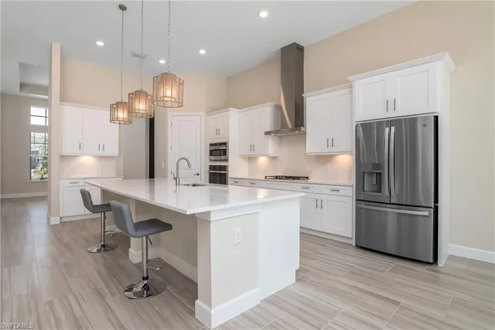 Kitchen with wall chimney range hood, tasteful backsplash, white cabinetry, an island with sink, and appliances with stainless steel finishes