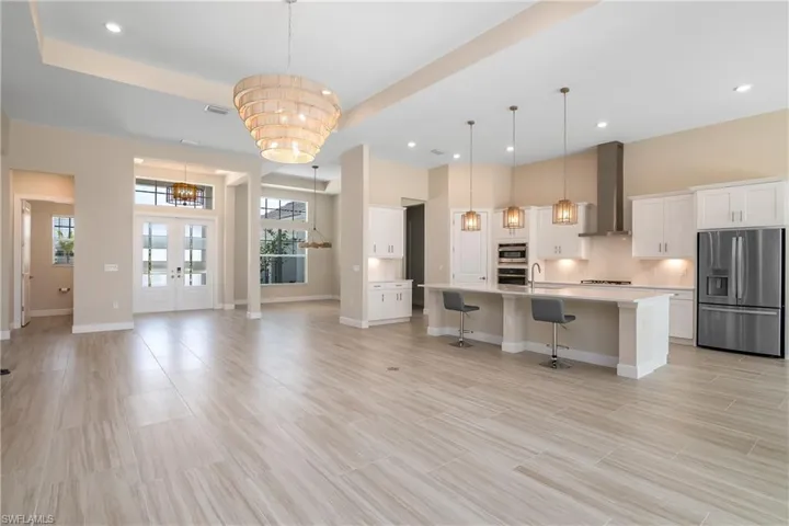 Kitchen with hanging light fixtures, appliances with stainless steel finishes, an island with sink, wall chimney exhaust hood, and a breakfast bar