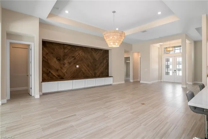Unfurnished living room with a raised ceiling, french doors, light tile flooring, and a chandelier