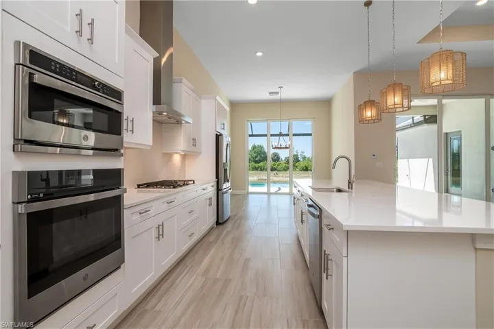 Kitchen with hanging light fixtures, sink, white cabinets, a kitchen island with sink, and appliances with stainless steel finishes