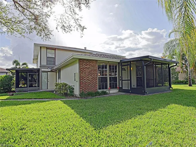 Exterior featuring a brick facade accent, two screened enclosures, light-toned siding, and a well-maintained lawn