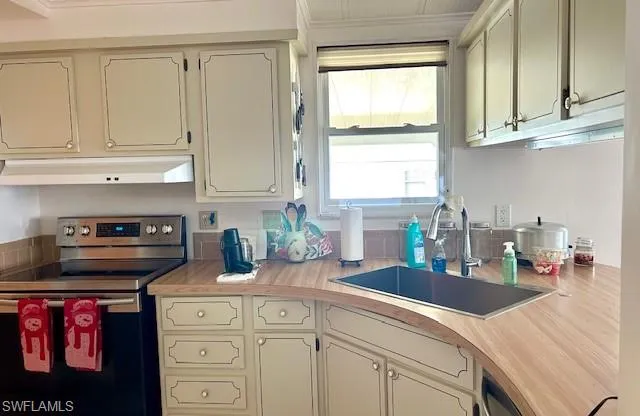 Kitchen with stainless steel electric range oven, light countertops, under cabinet range hood, and cream cabinets