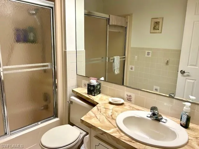 Bathroom featuring combined bath / shower with glass door, vanity, and backsplash