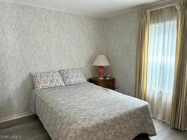 Bedroom with wallpapered walls and dark wood-type flooring