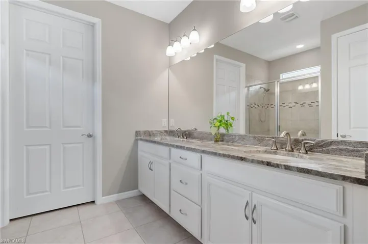 Bathroom featuring a sink, a stall shower, double vanity, baseboards, and tile patterned flooring