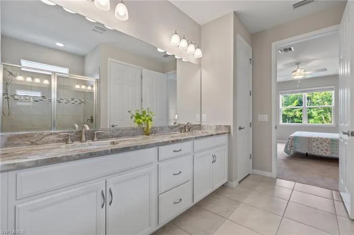 Ensuite bathroom with tile patterned floors, a sink, double vanity, a stall shower, and baseboards