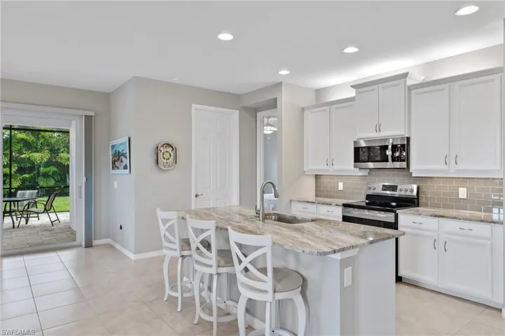 Kitchen featuring light stone counters, tasteful backsplash, a sink, an island with sink, and stainless steel appliances
