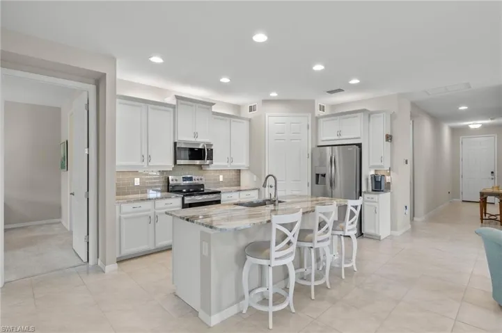 Kitchen with light stone counters, tasteful backsplash, a sink, a kitchen bar, and appliances with stainless steel finishes
