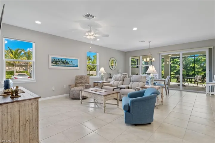 Living room featuring light tile patterned flooring, ceiling fan with notable chandelier, visible vents, and a healthy amount of sunlight